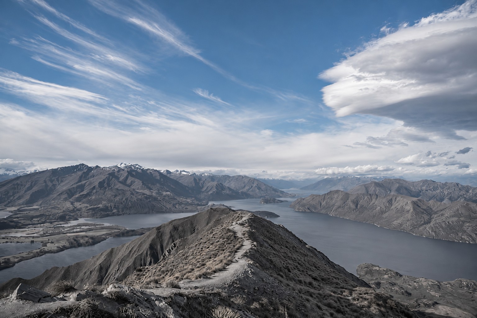 A mountain ridge overlooking a lake beneath drifting clouds